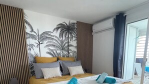 Moderni hotellihuone, jossa on suuri sänky, seinällä trooppinen seinämaalaus ja näkymä ulos liukuovien kautta.