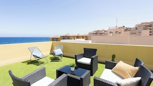 A rooftop terrace with wicker furniture, a cactus, and a view of the sea and buildings. - Home2Book Attic Terrace Apt Charming Ocean View (Las Caletillas)