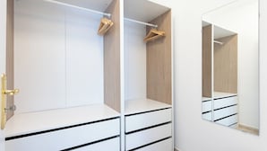 A walk-in closet with white drawers and a wooden interior, a mirror on the wall, and a door with a brass handle. - Home2Book Attic Terrace Apt Charming Ocean View (Las Caletillas)