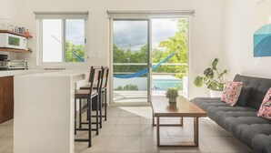 A modern kitchen with a dining area, a sofa, and a view of a pool through large sliding doors. - AQUA GUESTHOUSE 5~ A+ INTERNET ~ STEPS TO THE BEACH (Puerto Morelos)