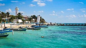 A coastal scene with boats docked near a lighthouse and beach. - AQUA GUESTHOUSE 5~ A+ INTERNET ~ STEPS TO THE BEACH (Puerto Morelos)
