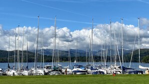 A marina with multiple sailboats docked, surrounded by green hills and a clear sky. - Ambleside Fell Rooms (Ambleside)