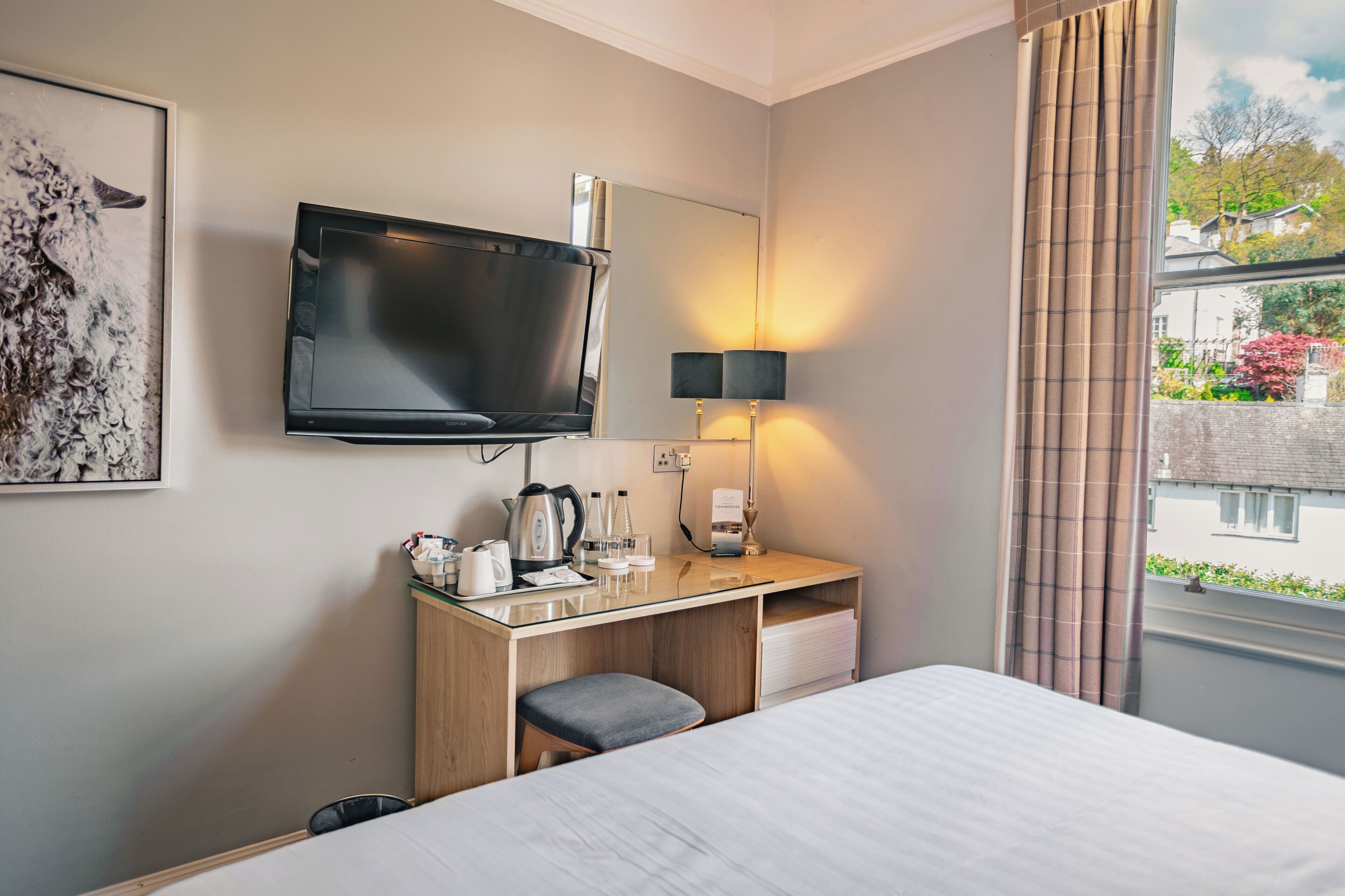 Een hotelkamer met een bed, een bureau met een flatscreen televisie, een lamp en een raam met gordijnen.