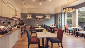A modern kitchen with a dining area, featuring a central island, multiple chairs, and a large window providing a view of the outdoors. - Ambleside Fell Rooms (Ambleside)