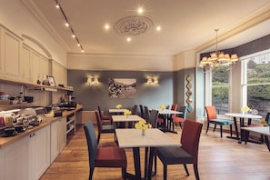 A modern kitchen with a dining area, featuring a central island, multiple chairs, and a large window providing a view of the outdoors. - Ambleside Fell Rooms (Ambleside)