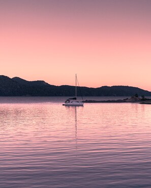 Ein Segelboot auf ruhigem Wasser, im Hintergrund ein rosafarbener Himmel.