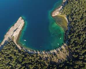 Luftaufnahme einer Küstenregion mit klarem, blauem Wasser, einem Sandstrand und dichten Wäldern.