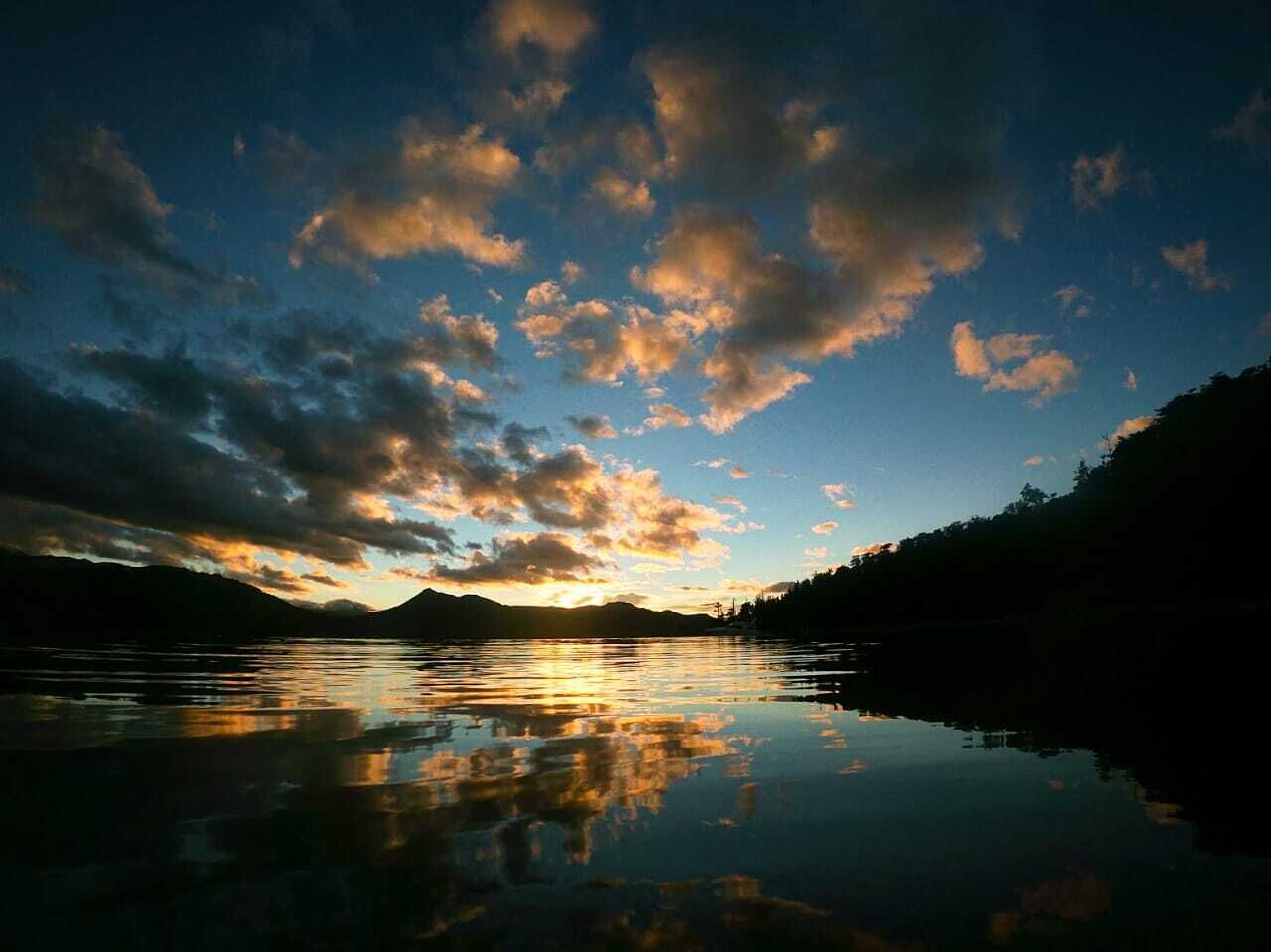 En rolig sø spejler himlen med skyer i solnedgangen.