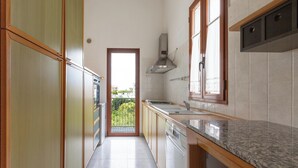 Une cuisine étroite avec des meubles en bois, une hotte de cuisine en acier inoxydable et, vue par une porte, un balcon.