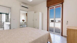 Ein Schlafzimmer mit Bett, Kleiderschrank, Badezimmer mit Waschbecken und einem Balkon mit Tür.