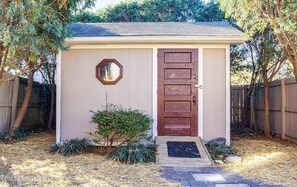 Simple entrance with a wooden door and step, surrounded by a wooden fence and lush greenery.