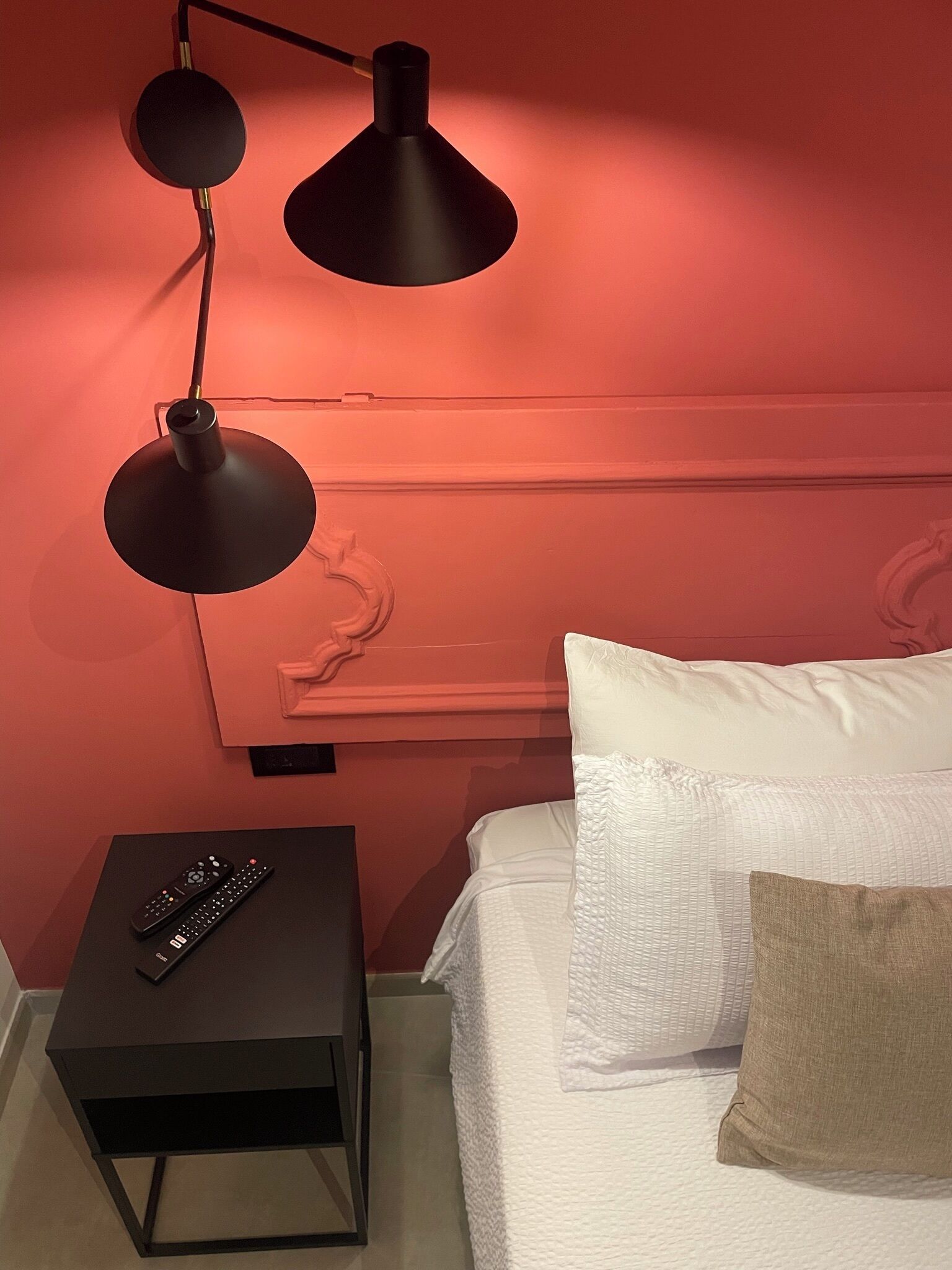 A bedroom with a bed, a nightstand, two black lamps, and a remote control.