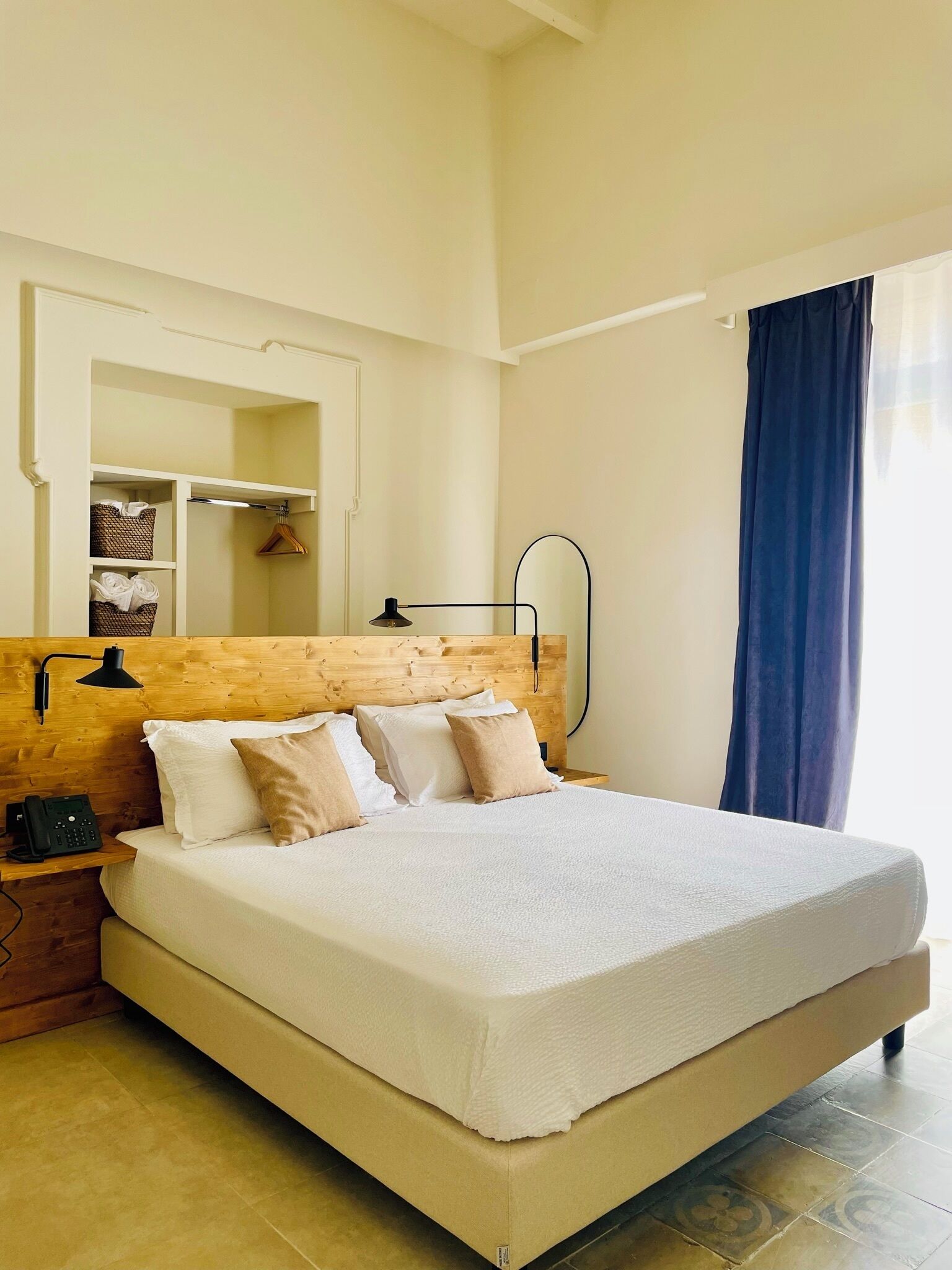 Una cama bien hecha con cabecera de madera, una lámpara de noche y un teléfono sobre una mesita de noche.