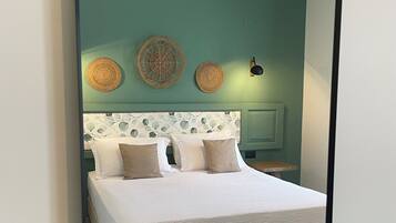 A neatly made bed with a patterned headboard, a wall-mounted light fixture, and two woven wall decorations.