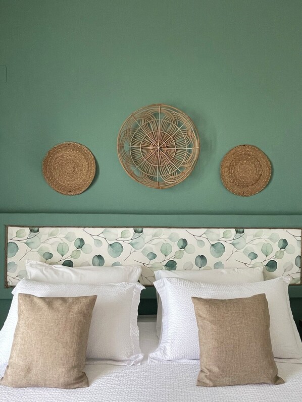 A bed with white and beige pillows, a green wall, and three woven wall hangings.