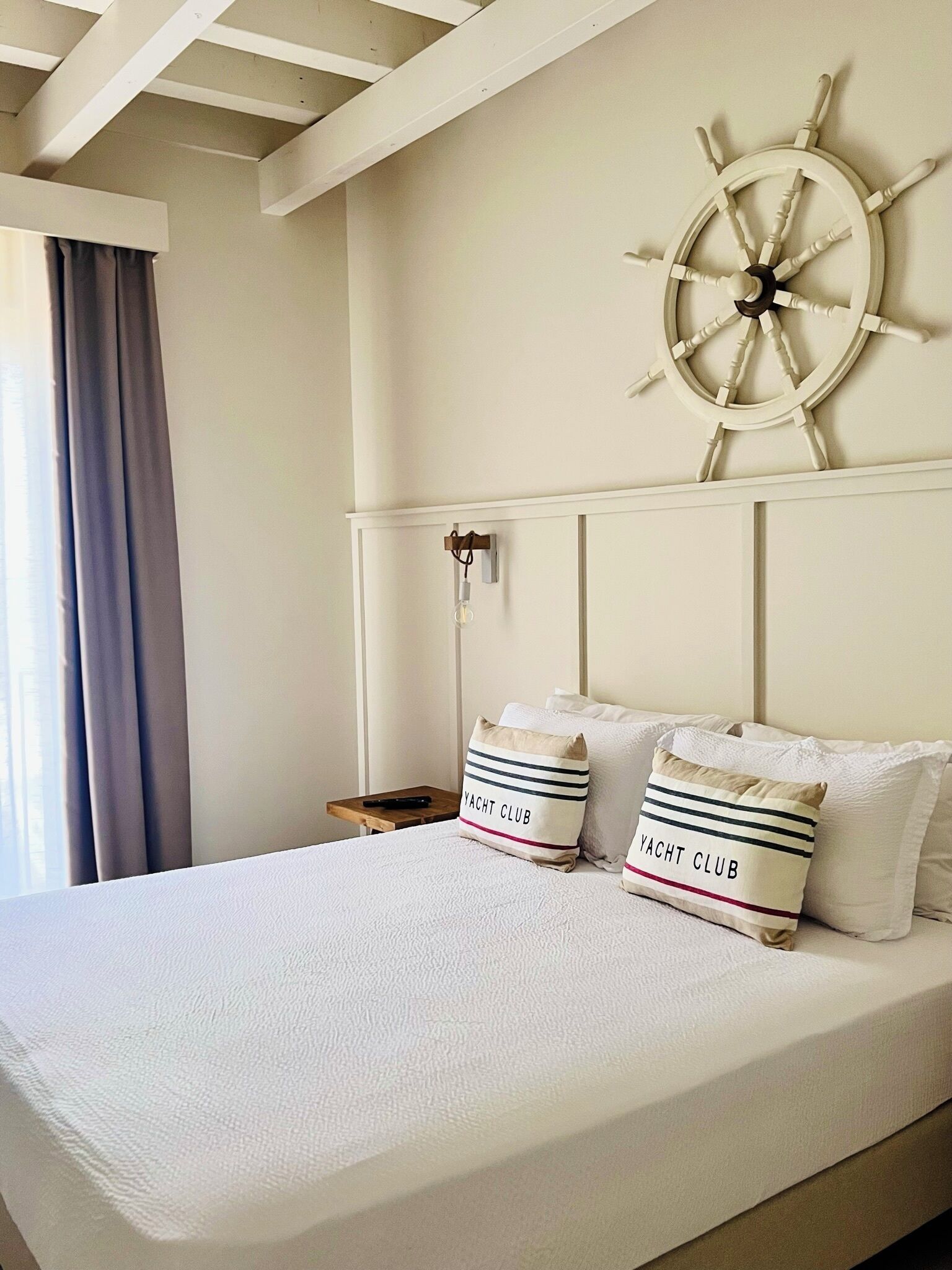 A bedroom with a bed, a ship's wheel wall decoration, and two pillows with 'YACHT CLUB' text.