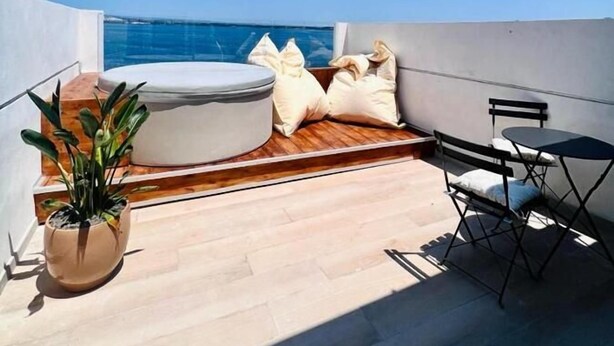 Une terrasse sur le toit avec un jacuzzi, un espace salon et un pot de fleurs.