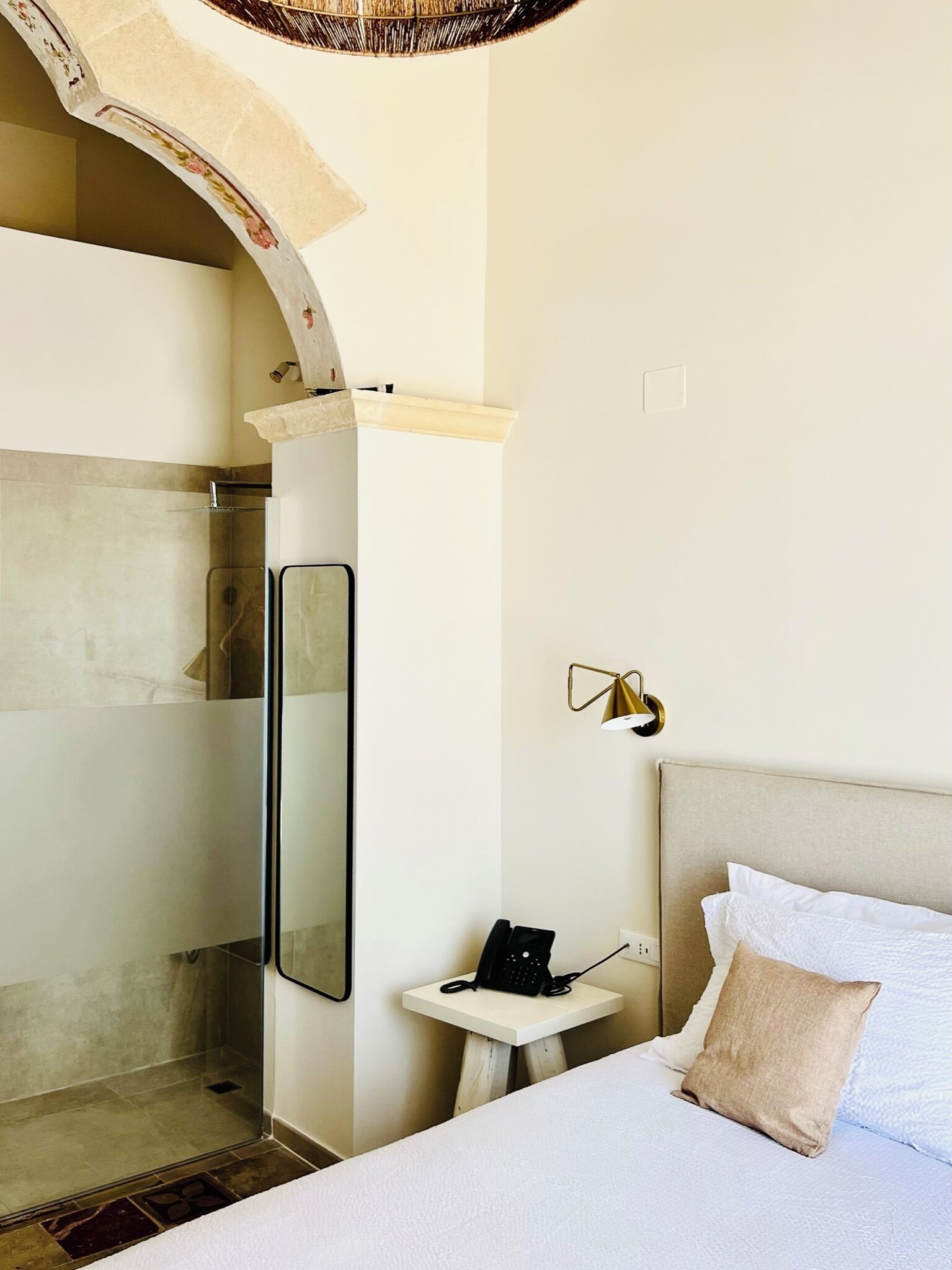 A hotel room with a bed, bedside table, phone, and a mirror.
