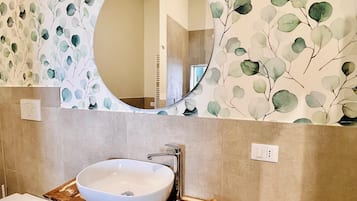 Un baño con un espejo redondo, un lavamanos blanco y un mueble de tocador de madera.