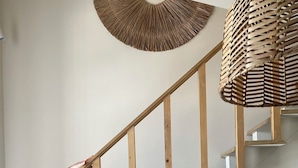 Un escalier en bois avec une rampe, une tapisserie murale tissée et un panier tressé suspendu au plafond.