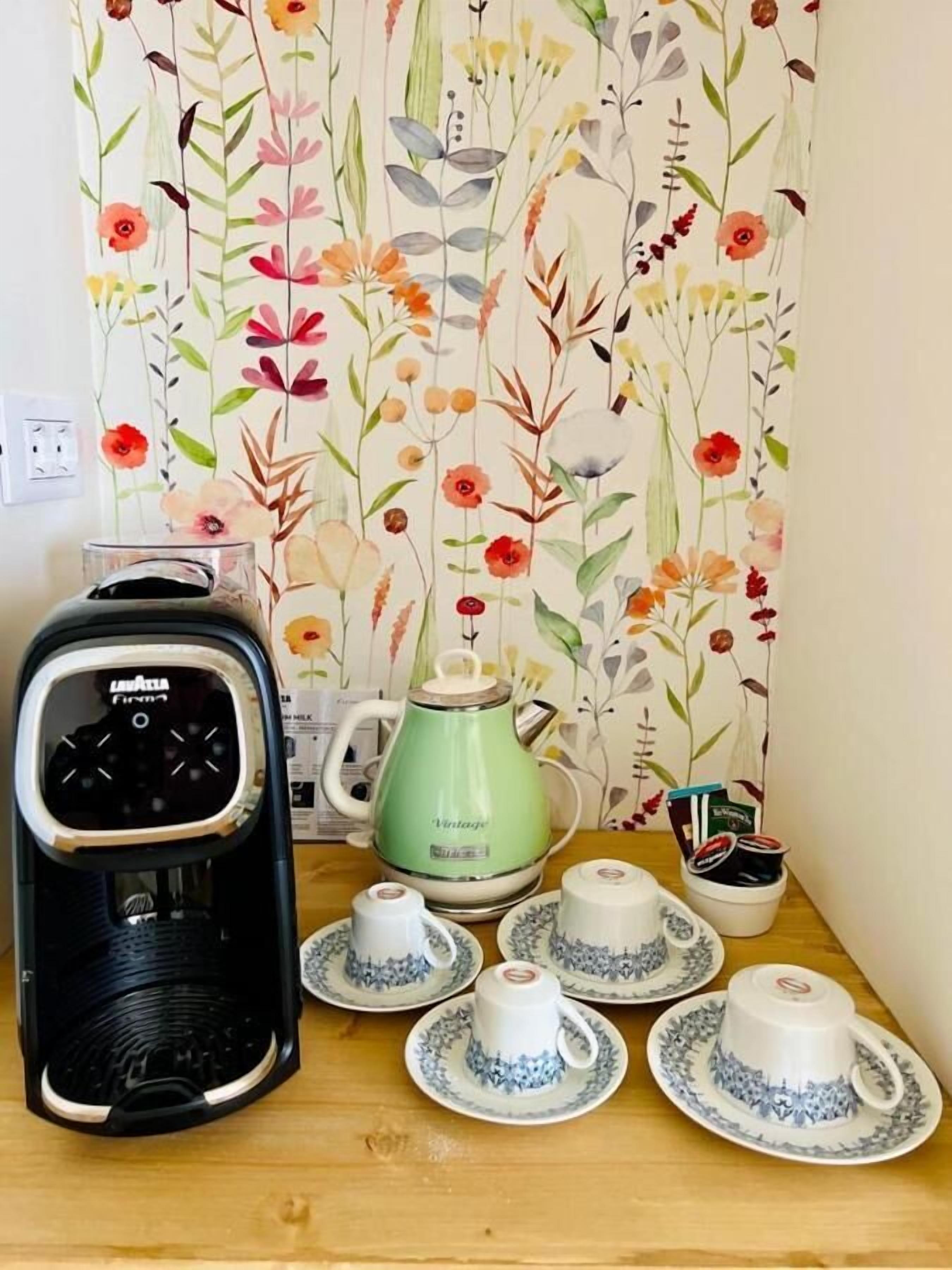 Eine Küchenzeile mit Kaffeemaschine, Wasserkocher und Teetassen auf einem Holztisch.