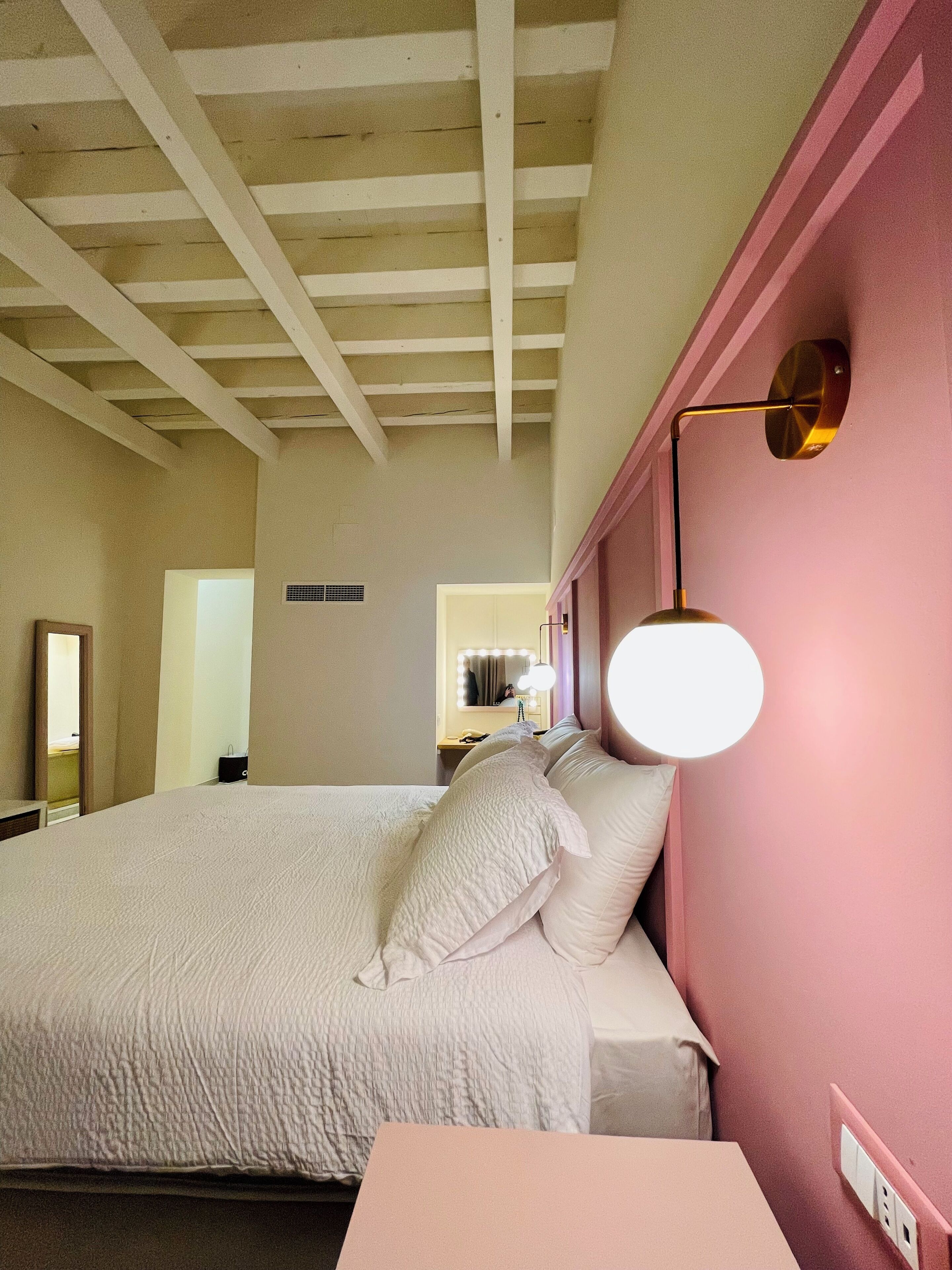Une chambre avec un grand lit, une table de chevet, une lampe fixée au mur et un miroir.