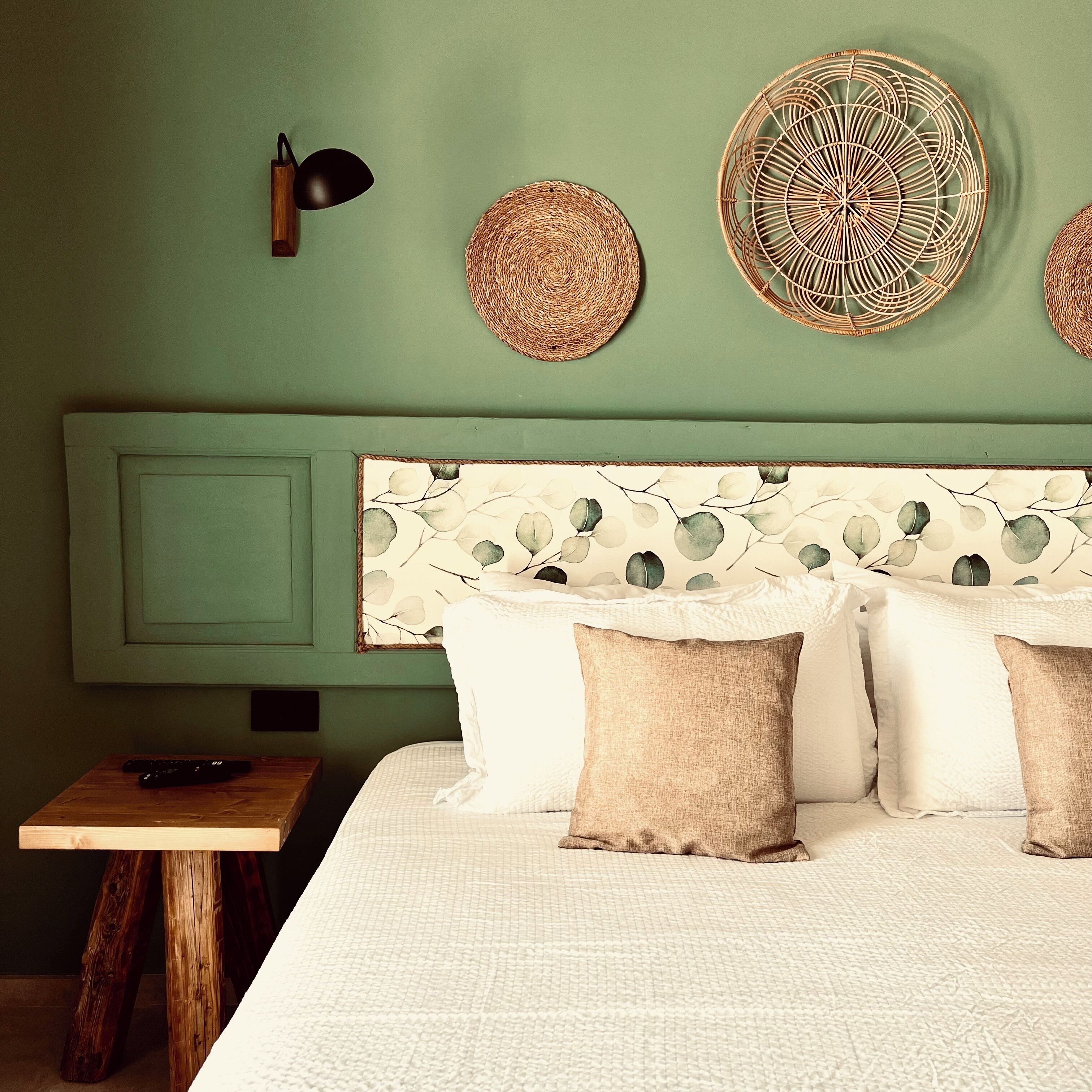A bedroom with a green wall, a woven headboard, and a wooden nightstand with a remote control.