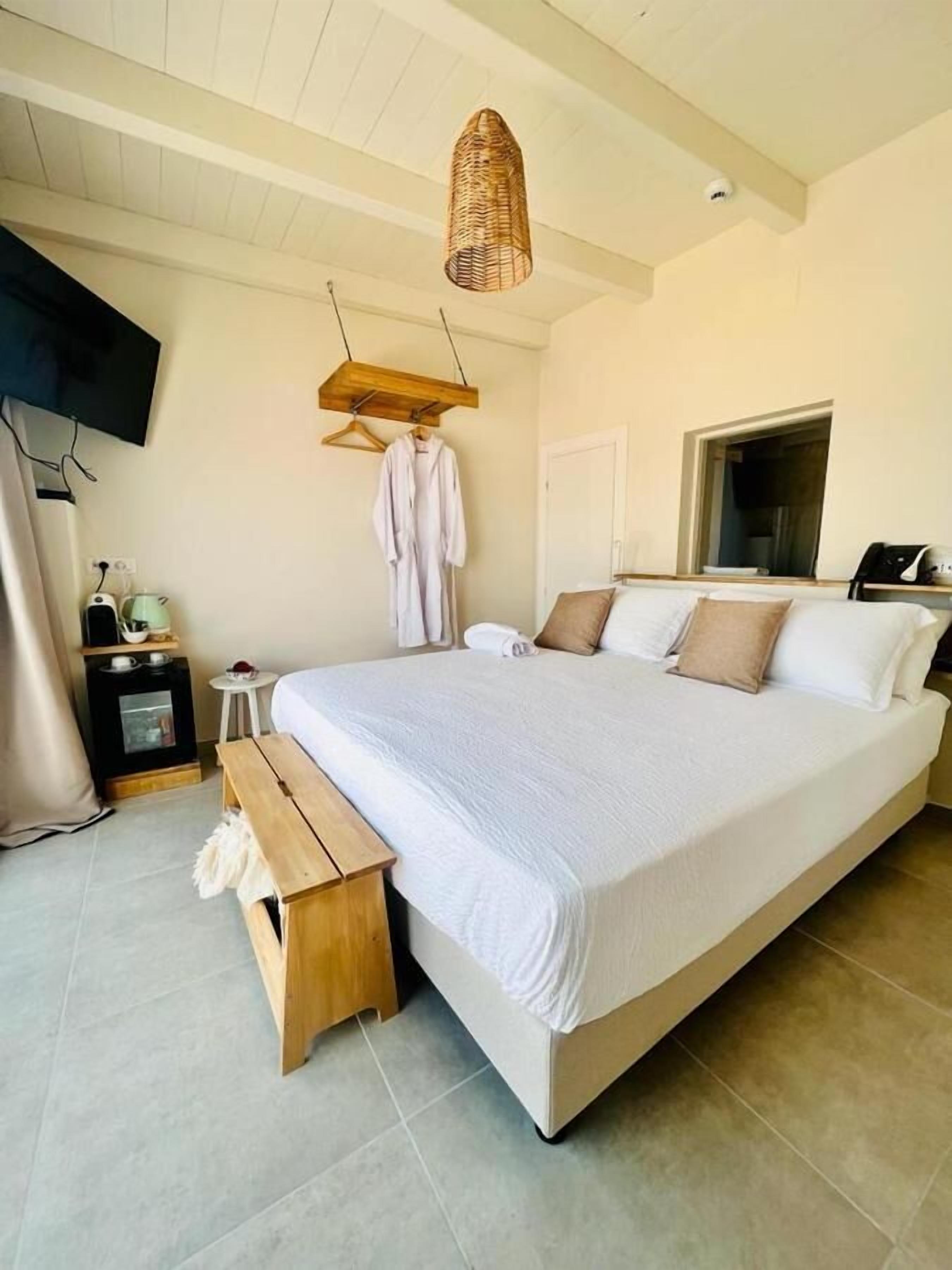 Ein geräumiges Schlafzimmer mit einem großen Bett, einer Holzbank, einer hängenden Leuchte, einem an der Wand montierten Fernseher und einem kleinen Tisch mit einem Wasserkocher.