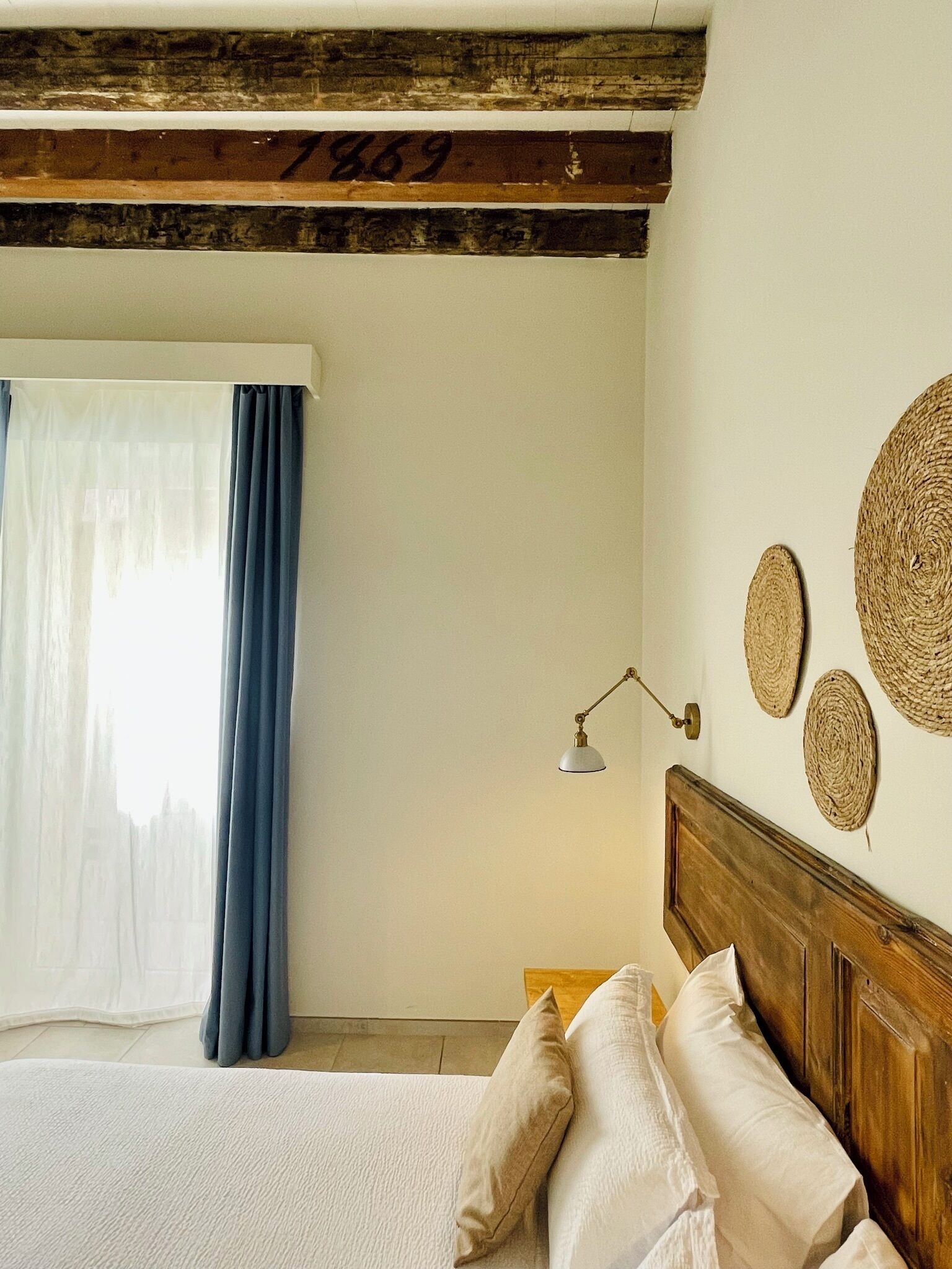 Un dormitorio con cama, mesita de noche, lámpara y ventana con cortinas.
