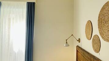 Un dormitorio con cama, mesita de noche, lámpara y ventana con cortinas.