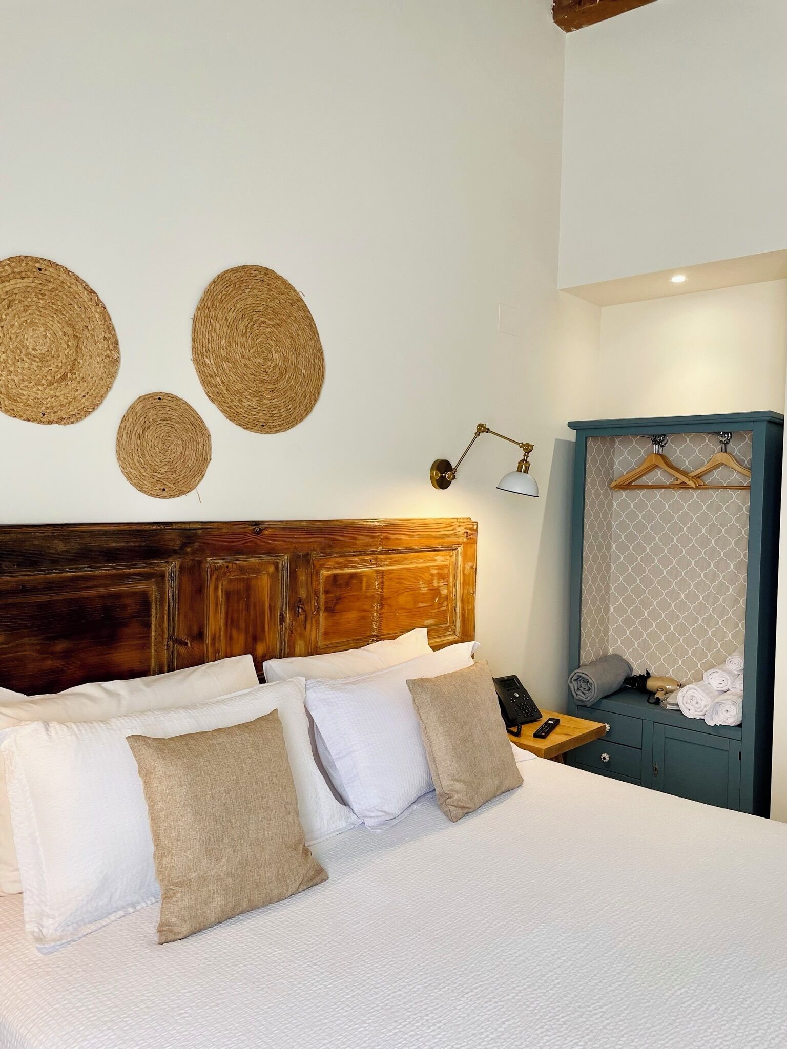 A neatly made bed with white and beige pillows, a wooden headboard, and three woven wall hangings.