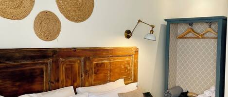 A neatly made bed with white and beige pillows, a wooden headboard, and three woven wall hangings.