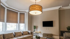 A living room with a beige sofa, a wooden coffee table, a TV mounted on the wall, and a window with blinds. - Church View (Scarborough)
