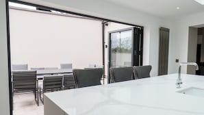 A modern kitchen with a white marble countertop, a built-in sink, and a large sliding glass door leading to an outdoor seating area. - Church View (Scarborough)
