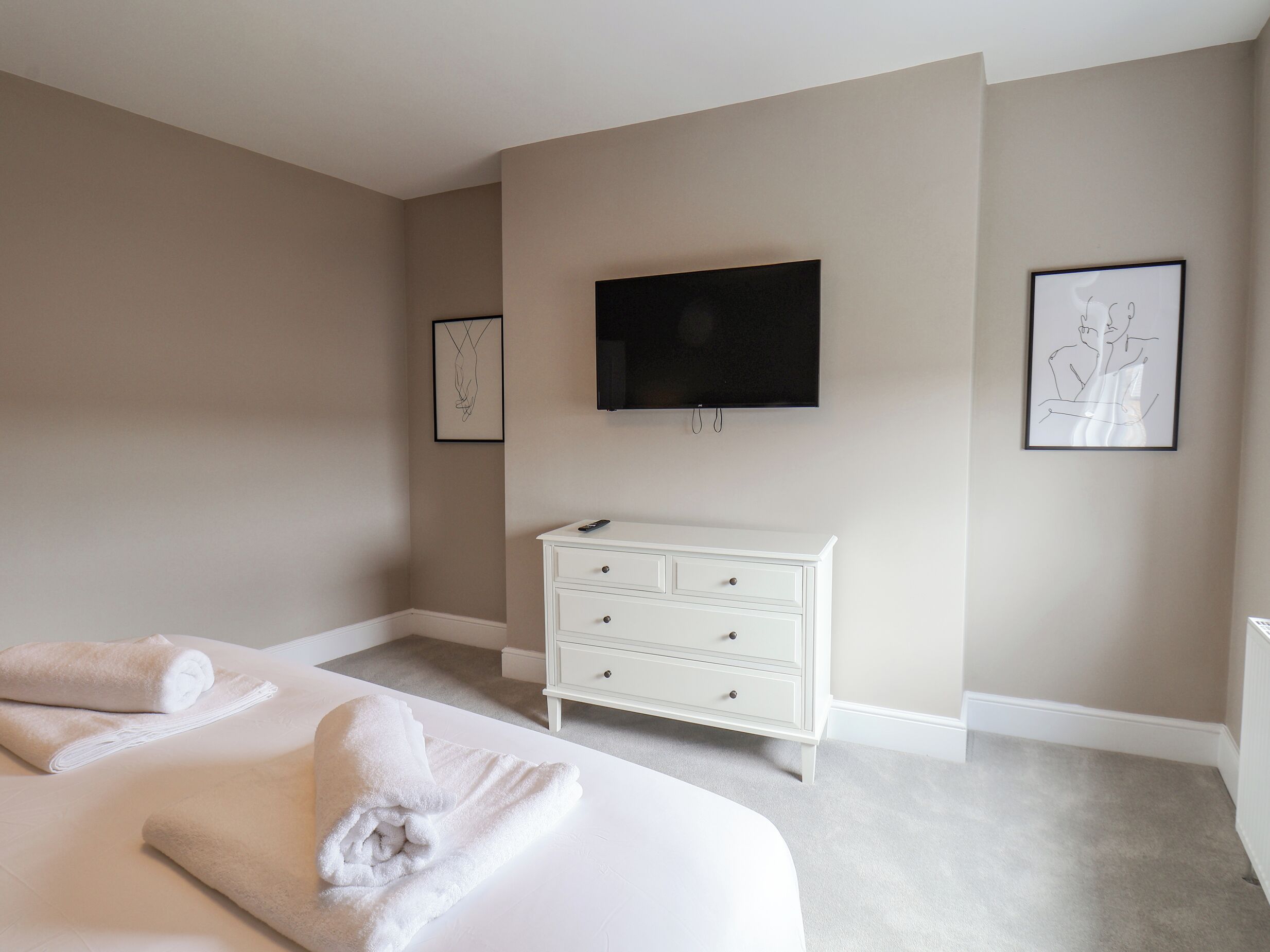 Een slaapkamer met een bed, een witte dressoir, een flatscreen televisie en twee ingelijste kunstwerken aan de muur.