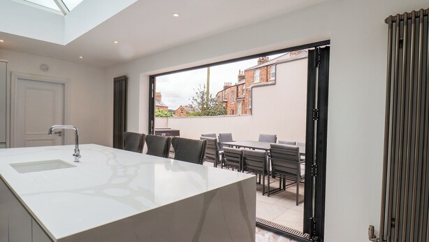 A modern kitchen with a large island, a dining area with chairs, and a view of the neighborhood through the open door. - Church View (Scarborough)