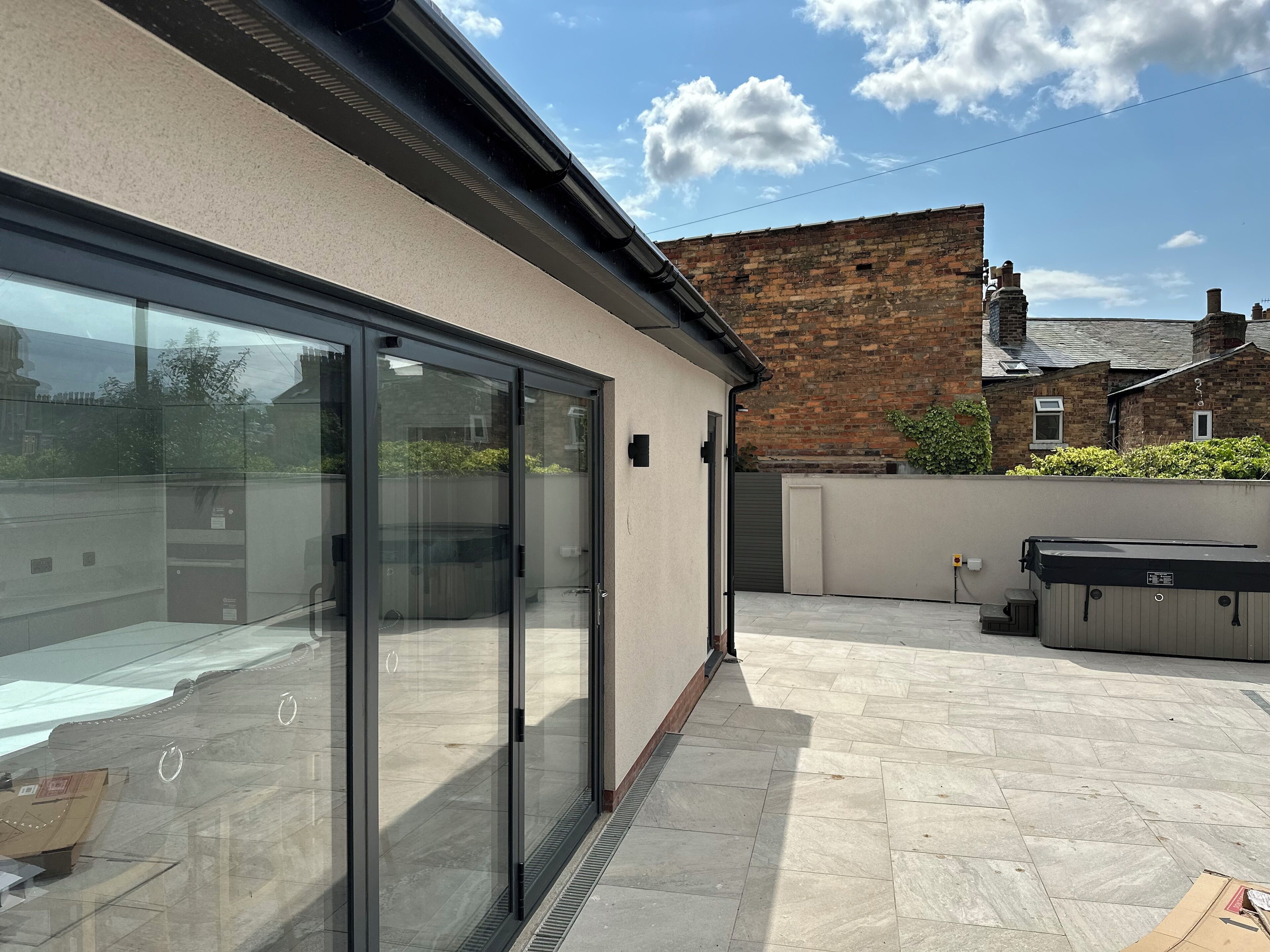 A modern building with large glass doors, a tiled patio, and a brick wall in the background.