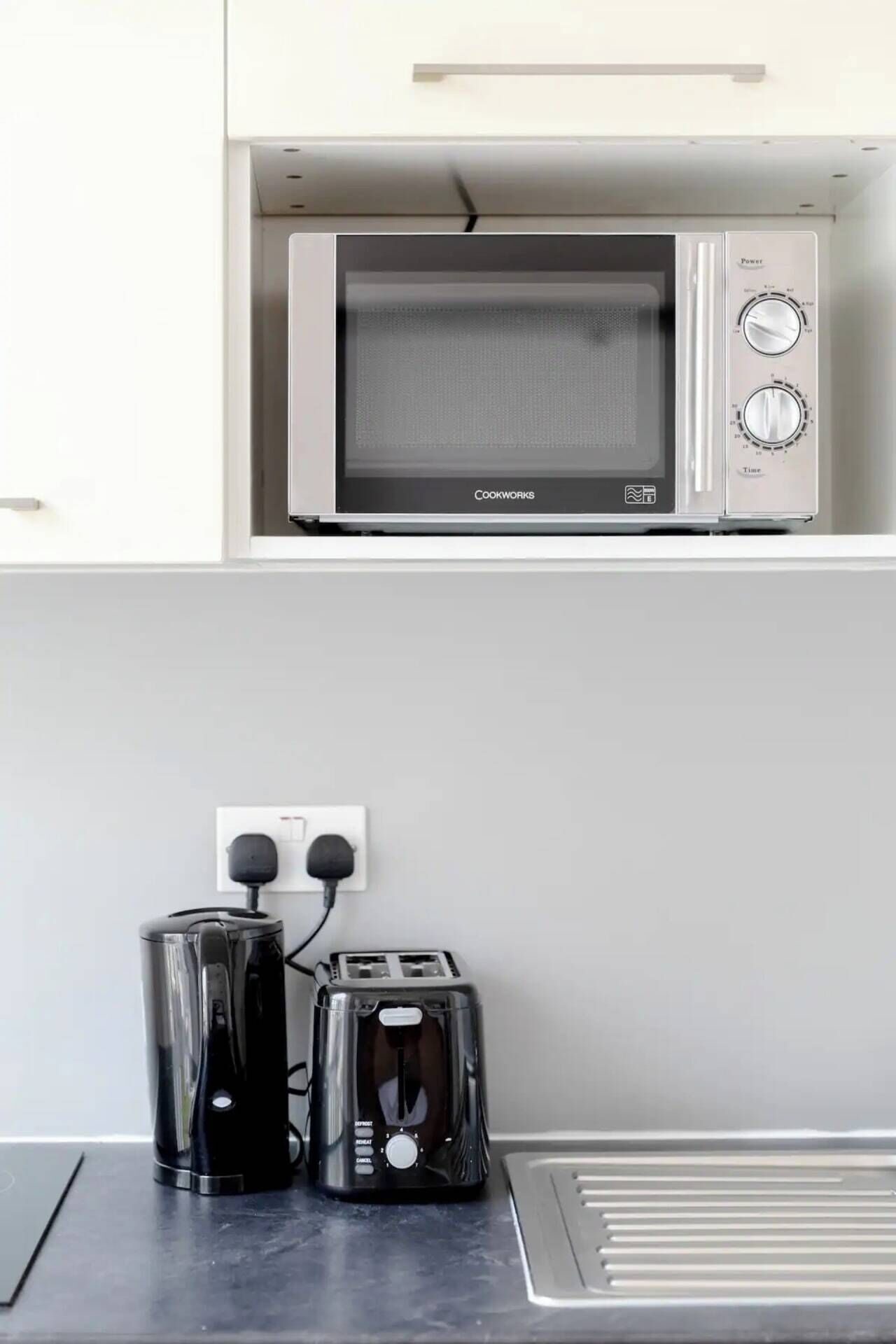 Cozinha compacta com micro-ondas embutido, chaleira e torradeira em bancada.