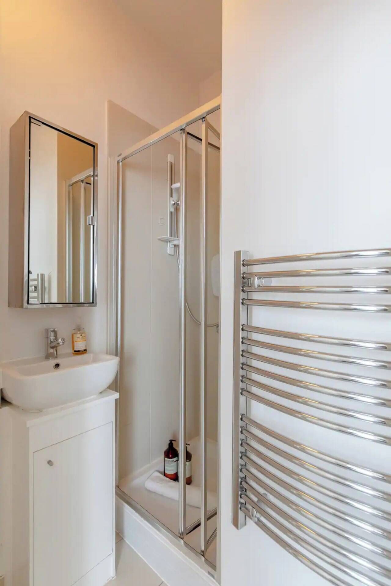 A modern bathroom with a glass-enclosed shower, a white sink, a mirror, and a towel rack.