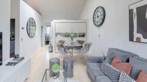 A modern living room with a grey sofa, a dining table with chairs, and a kitchen area in the background. - Stylish 1BD Flat 5 Mins to Harrods- Knightsbridge (London)