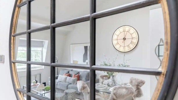 A living room with a modern design, featuring a sofa, coffee table, and a decorative clock on the wall. - Stylish 1BD Flat 5 Mins to Harrods- Knightsbridge (London)