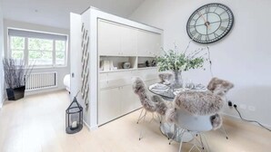 A modern kitchen with white cabinetry, a dining table set for four, and a decorative clock on the wall. - Stylish 1BD Flat 5 Mins to Harrods- Knightsbridge (London)