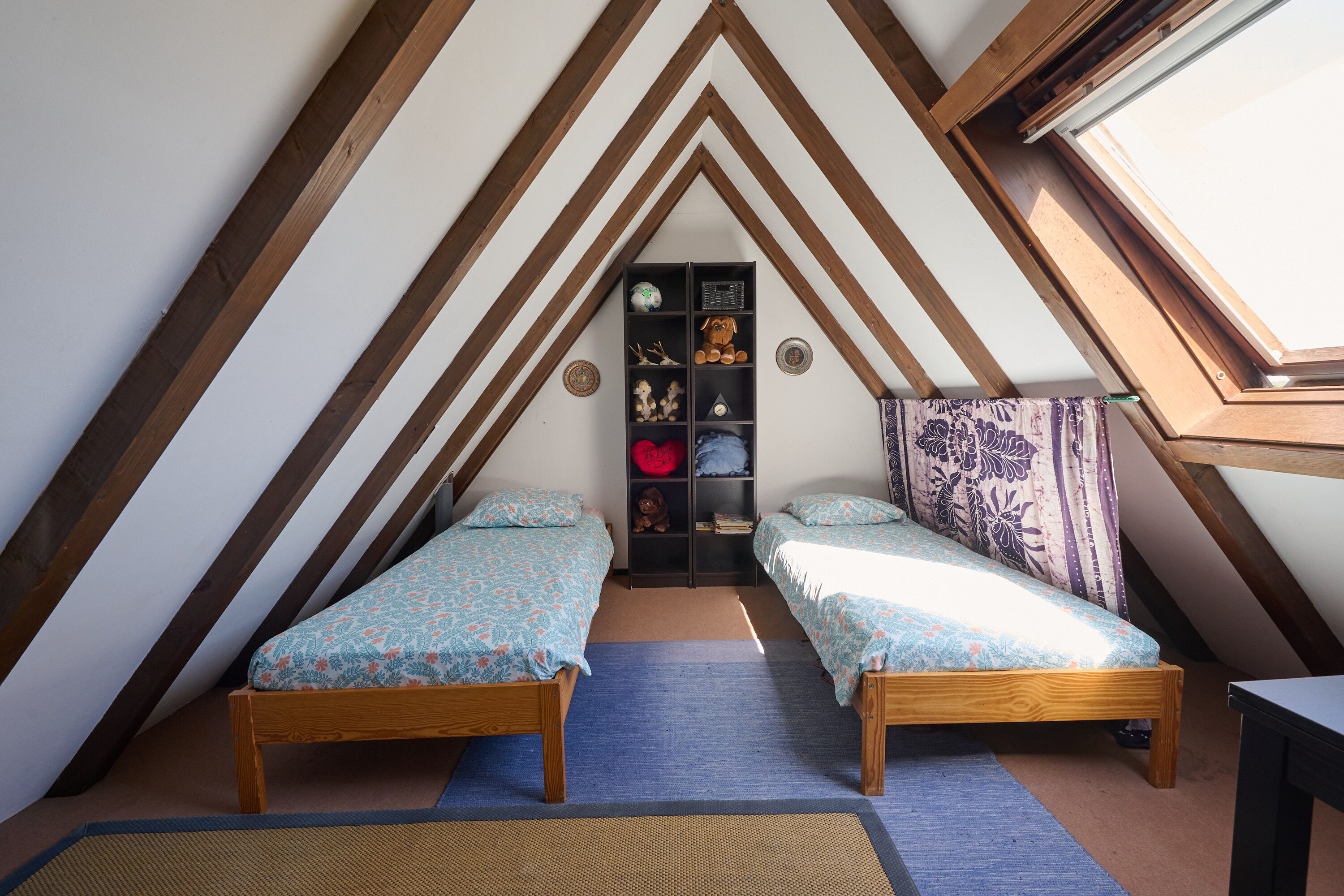A small attic bedroom with two wooden beds, a built-in bookshelf, and a skylight.