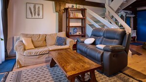A living room with a sofa, a recliner, a coffee table, a bookshelf, and a staircase. - Le Tonneau Bleu - Appt avec piscine partagée (Lembach)