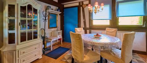 A dining area with a round table, four chairs, a white cabinet with glass doors, a blue door, and a chandelier.