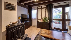 A cozy living room with a wooden bench, a television, and a cabinet. - Le Tonneau Bleu - Appt avec piscine partagée (Lembach)