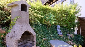 A stone-built outdoor oven with a chimney, surrounded by lush greenery and a statue. - Le Tonneau Bleu - Appt avec piscine partagée (Lembach)