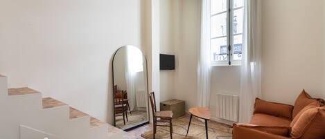Una sala de estar moderna con una escalera, un sofá, una mesa con tetera, un espejo y una ventana con cortinas.