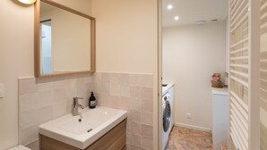 A modern bathroom with a sink, mirror, and a washing machine in the adjacent room.