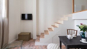 A modern interior with a staircase, a flat-screen TV, a dining table with white tableware, and a wicker basket.